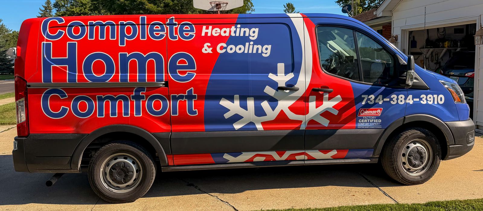 A red, white and blue Complete Home Comfort service van parked in a driveway.