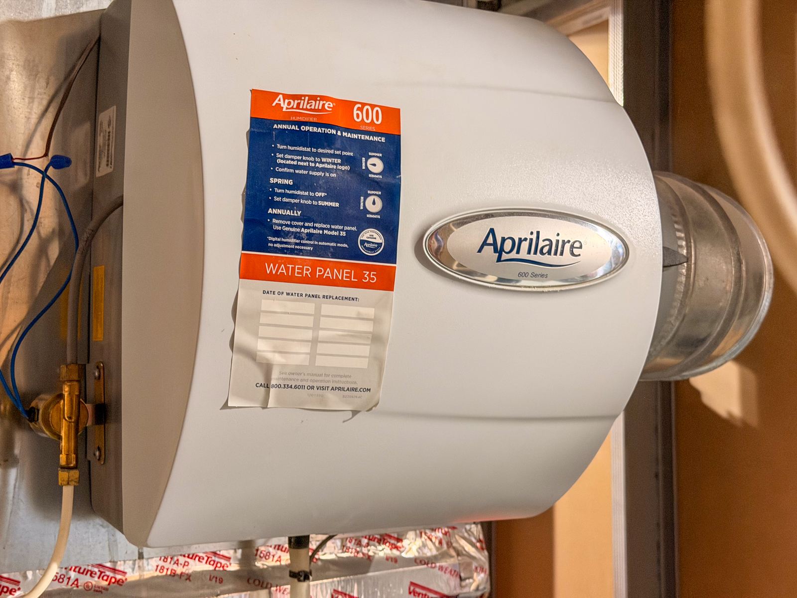 A whole-home humidifier mounted on furnace ductwork, with its maintenance instruction label visible.